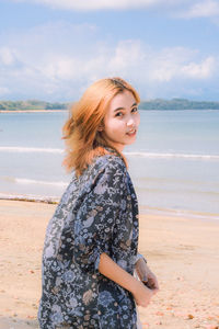 Side view of young woman standing on beach against sky