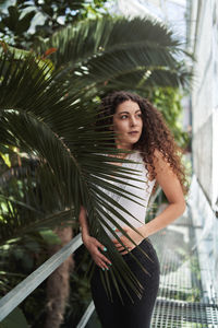 Young woman looking away standing by railing against trees