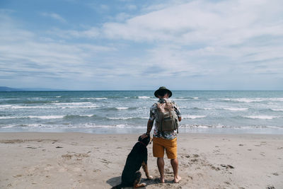 Back traveler man with backpack and dog on the beach