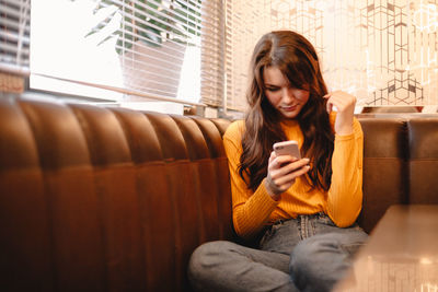 Young woman using smart phone while sitting in cafe