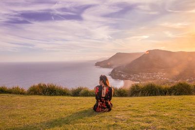 Rear view of woman sitting on field against sea