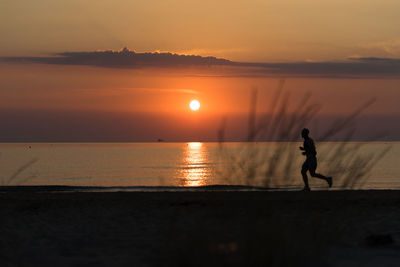 Silhouette man standing on sea against sky during sunset