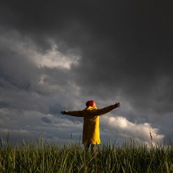 Man in yellow raincoat with spreading hands wide open standing on the field in rainy weather