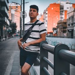 Young man on railing against buildings in city