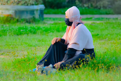 Rear view of women sitting on field with cat