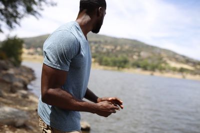 Side view of young man standing on rock against sky