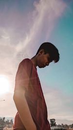 Side view of young man standing against sky