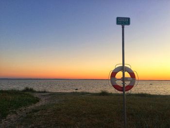 Warning sign on beach against sky during sunset