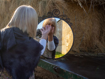 Reflection of woman gesturing in mirror by hay bales