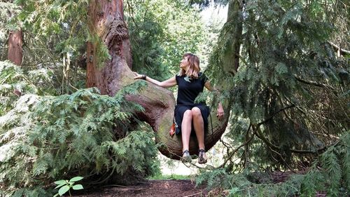 Young woman sitting on tree trunk in forest