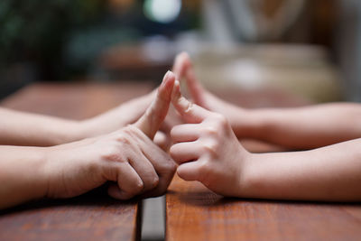 Cropped hand of mother and daughter touching finger on wooden table