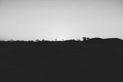 Silhouette trees on field against clear sky