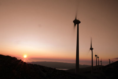 Silhouette windmill on landscape against sky during sunset