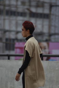 Side view of young man looking away against building