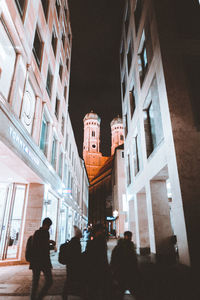 People walking on illuminated street amidst buildings at night