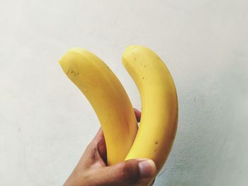Close-up of cropped hand holding bananas against wall