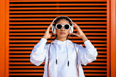 Young african american woman with braided hair wearing urban sportswear with headphones and sunglass