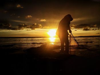 Silhouette man standing on beach against sky during sunset