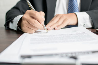 Midsection of businessman signing contract paper at desk in office