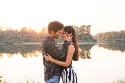 Young couple standing by lake against sky