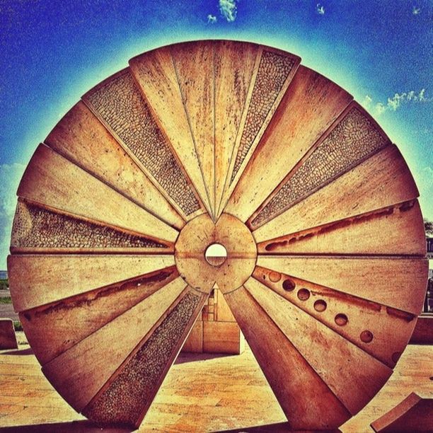 circle, wood - material, geometric shape, blue, sky, wheel, pattern, no people, low angle view, built structure, outdoors, sunlight, day, wooden, wood, shape, arts culture and entertainment, cloud - sky, part of, red