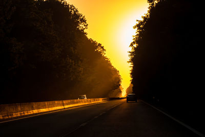 Road amidst trees against sky during sunset