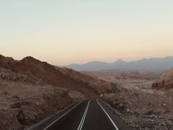 Road leading towards mountains against clear sky