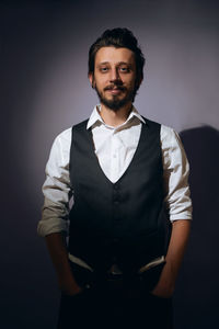 Stylish hipster man with a beard stands in the background in the studio in a vest and white shirt