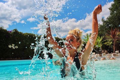 Cheerful young woman swimming in pool against cloudy sky during sunny day