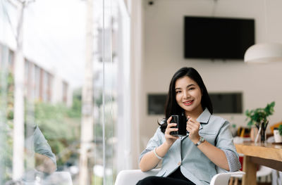 Portrait of young businesswoman holding coffee cup sitting at office