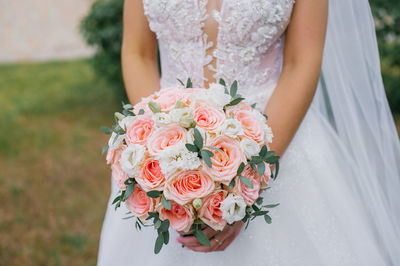 A bride with a wedding bouquet of roses and carnations in her hands on the background 