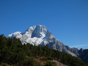 Low angle view of snowcapped mountains against clear blue sky