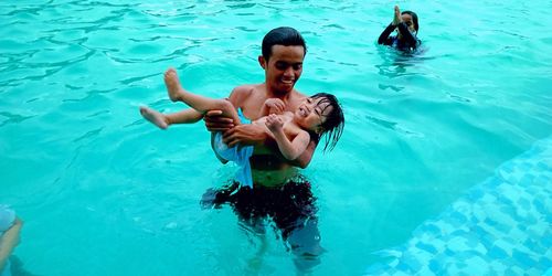 High angle view of girl with father holding daughter swimming in pool