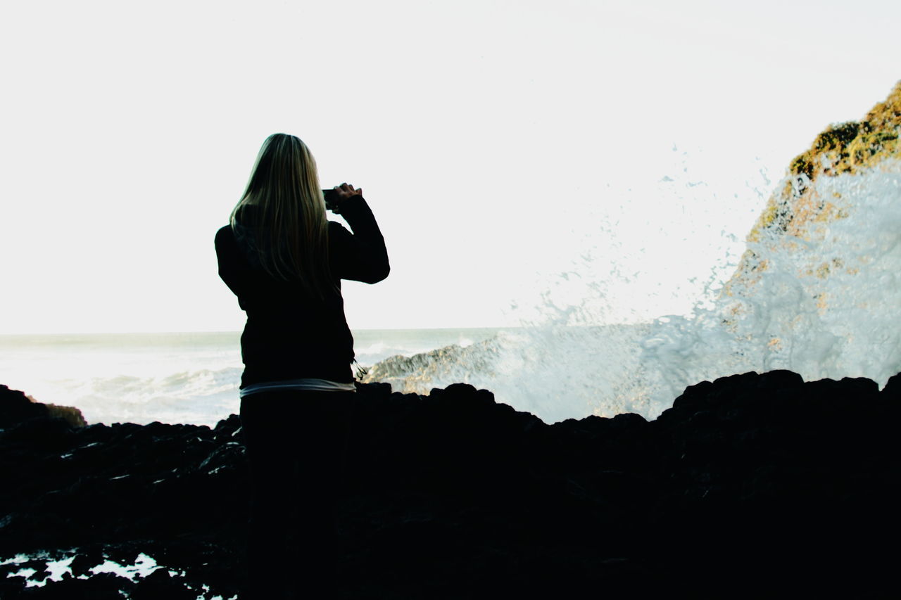 sea, water, horizon over water, lifestyles, standing, leisure activity, rear view, scenics, silhouette, tranquil scene, tranquility, beauty in nature, person, full length, getting away from it all, nature, looking at view, beach