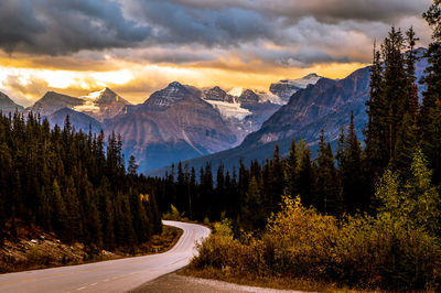 Road amidst trees and mountains against sky during sunset