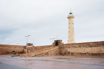 Lighthouse by building against sky