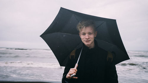 Portrait of man holding camera while standing on beach