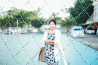 Portrait of young woman standing on court seen through net