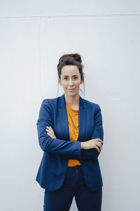 Confident businesswoman with arms crossed standing in front of white wall