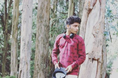 Young man standing by tree trunk