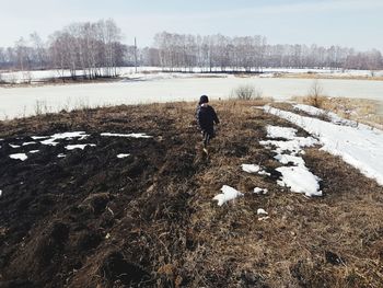 Rear view of person walking on snow covered field