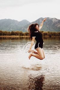 Young woman jumping in lake against sky