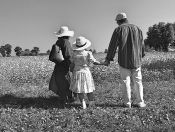 Rear view full length of family standing on field against sky