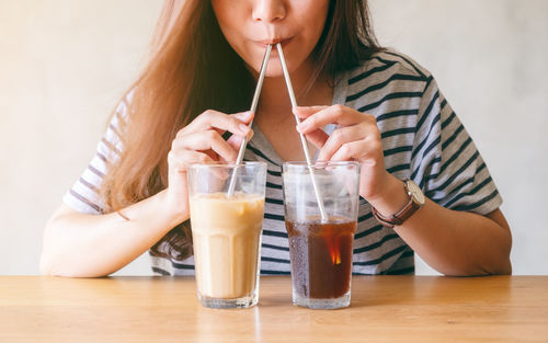 Midsection of woman drinking glass with drink on table