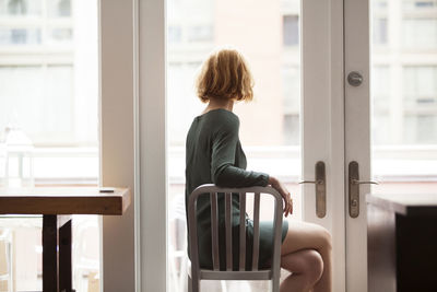 Woman sitting on chair and looking through window at home