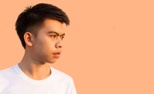 Portrait of young man looking away against orange background