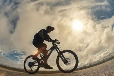 Low angle view of man riding bicycle on road against sky