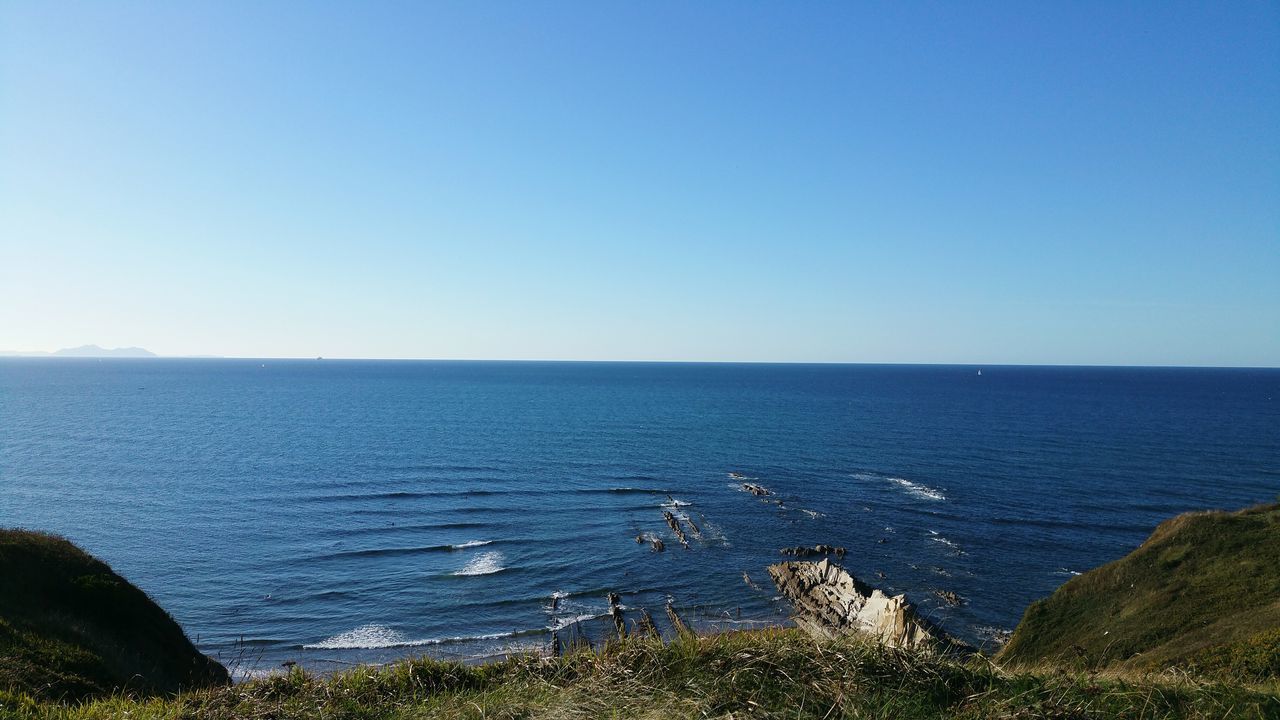 water, sea, clear sky, horizon over water, tranquil scene, copy space, tranquility, scenics, beauty in nature, blue, nature, idyllic, coastline, grass, seascape, non-urban scene, remote, calm, outdoors, shore