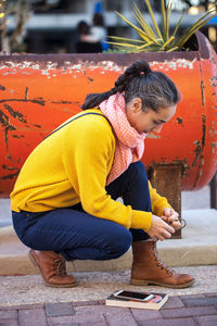 Side view of woman tying shoelace while crouching on footpath