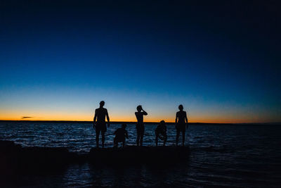 Silhouette people on beach against clear sky during sunset